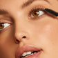 Close-up of a woman's face with mascara and a makeup product on a white background